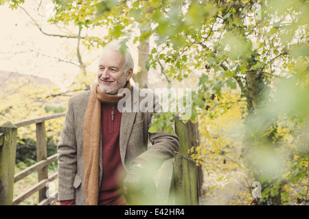 Senior man leaning on wooden fence, smiling Banque D'Images