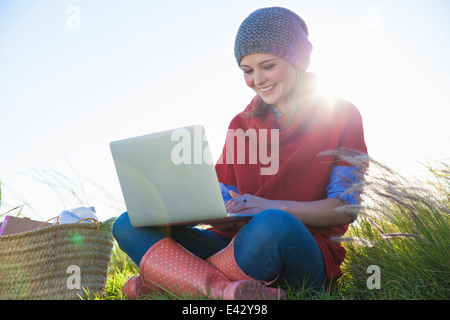 Young woman using laptop assis dans l'herbe haute Banque D'Images