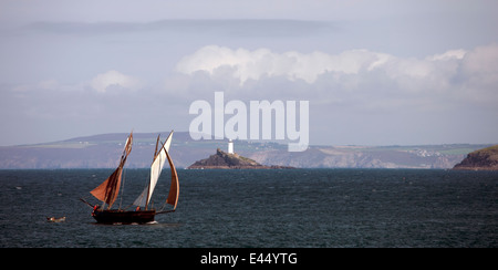 Une ancienne ligne, Cornish, bateau de pêche à voile à travers la baie de St Ives, Cornwall, UK, avec phare de Godrevy dans l'arrière-plan. Banque D'Images