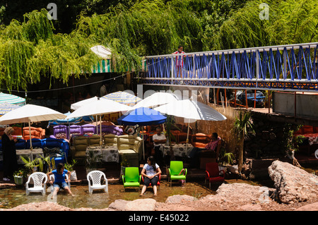 Tables, chaises de patio en plastique avec des parasols dans les restaurants sur les rives de la rivière de l'Ourika, la vallée de l'Ourika, Atlas, Maroc Banque D'Images