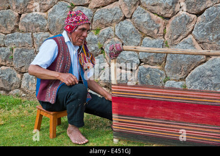 Un homme âgé portant un chapeau, en vêtements traditionnels indiens Quechua, assis sur le plancher travaillant sur la civière d'un métier Banque D'Images