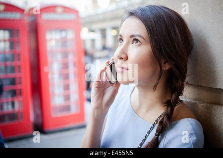 Jeune femme sur smartphone, en face de la cabine téléphonique de Londres Banque D'Images