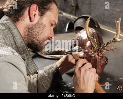 Marteau de forgeron sur cuivre sculpture de cerf en atelier Banque D'Images