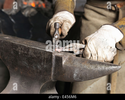 Image recadrée de forgerons hands hammering hot metal rouge Banque D'Images