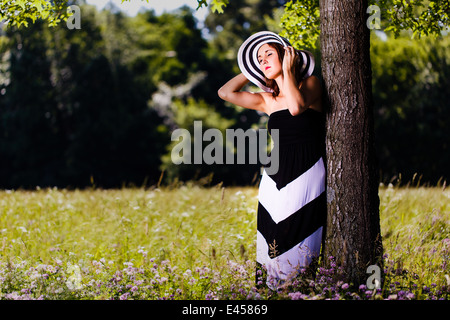 Une belle jeune femme au soleil alors qu'elle s'appuie contre un arbre. Banque D'Images