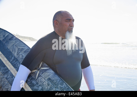 Mâle mature surfer strolling on beach with surfboard Banque D'Images