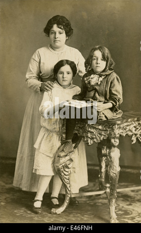 Photographie Ancienne vers 1910, studio image d'une mère et ses deux filles, l'une tenant un livre. Banque D'Images