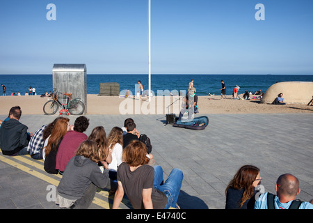 Les gens écoutent de musicien ambulant qui joue de la guitare sur la promenade de la Barceloneta à Barcelone, Catalogne, Espagne. Banque D'Images
