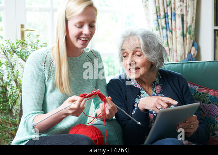 Grand-mère avec tablette numérique montrant sa petite-fille comment tricoter Banque D'Images