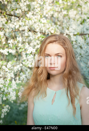 Belle jeune fille aux cheveux blonds dans le jardin en fleurs de printemps Banque D'Images