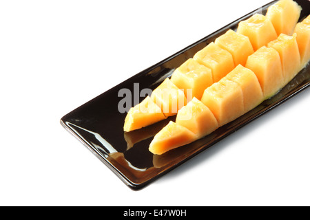 Melon cantaloup tranches de fruits dans un plat noir sur fond blanc. Banque D'Images