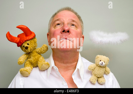 Homme avec un diable sur une épaule et un ange sur l'autre à la recherche vers le ciel. Banque D'Images