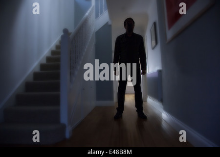 Silhouette d'un homme debout, dans un couloir d'une maison avec les escaliers à sa droite. Banque D'Images