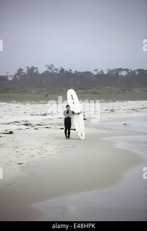 Surfer en combinaison de plongée se trouve sur la plage de sable littoral avec planche de surf à Pacific Grove par Pebble Beach en Californie Banque D'Images