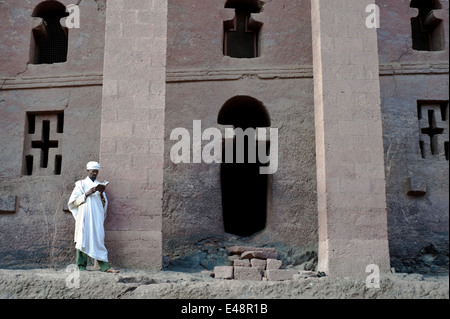 Prêtre orthodoxe, la lecture d'un livre religieux en face d'un rocher taillé eglise (Éthiopie) Banque D'Images