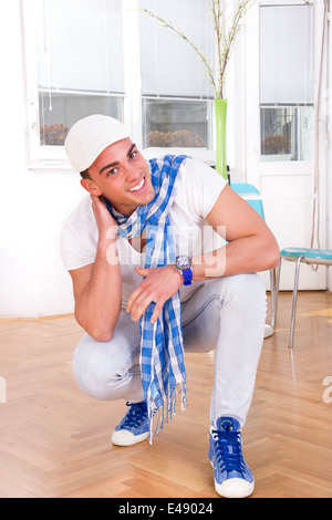 Smiling handsome mode homme avec un foulard et casquette blanche posant dans le salon Banque D'Images