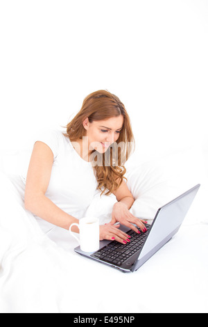 Angle view of woman using laptop computer in bed avec tasse de café de côté Banque D'Images