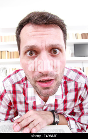 Close up of nutty confus et choqué le professeur ou étudiant avec livre dans ses mains, l'ambiance de salon avec bibliothèque historique Banque D'Images