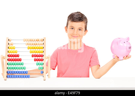 Boy holding a piggybank assis à une table avec un boulier Banque D'Images