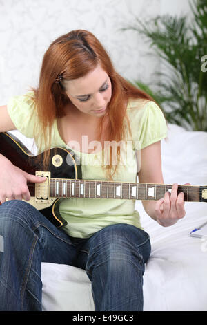 Jeune fille qui joue de la guitare assis sur un lit Banque D'Images