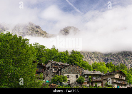 Petit groupe de maisons anciennes en pierre entre des montagnes et des forêts dans les Alpes italiennes. Banque D'Images