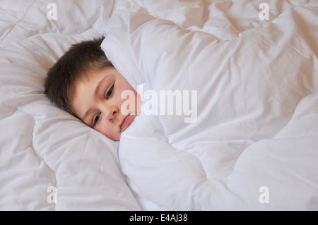 Écolier garçon malade sept ans se trouve mis lit blanc couverture réfléchie un triste pleure Banque D'Images