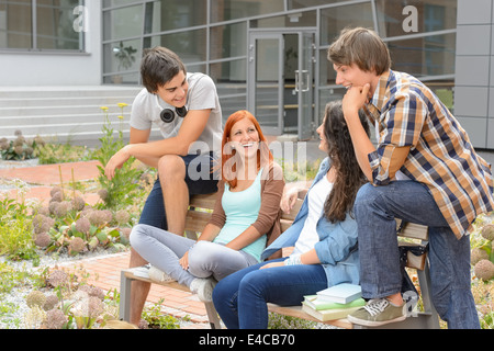 Amis étudiants assis sur un banc à l'extérieur du campus de l'université rire chatting Banque D'Images