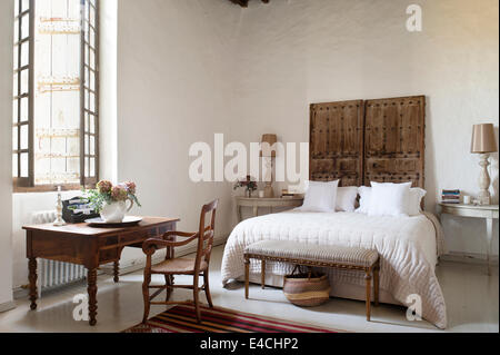 Ancienne paire de portes cloutées derrière lit dans la grande chambre blanche avec un bureau en bois Banque D'Images