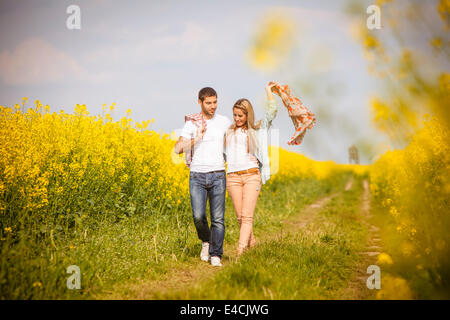 Jeune couple en train de marcher le long du chemin de champ par champ de colza, Toscane, Italie Banque D'Images
