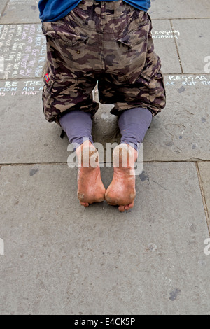 Un homme sans-abri aux pieds nus s'agenouille sur le trottoir pour écrire ses paroles de sagesse dans les rues de Camden Town, à Londres. Banque D'Images