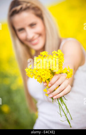 Blond woman holding out bouquet de fleurs de colza, Toscane, Italie Banque D'Images