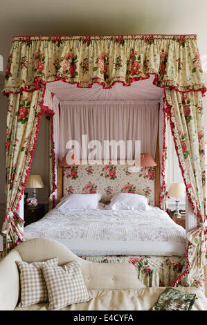 Une chaise au pied d'un lit à baldaquin avec des rideaux de chintz Banque D'Images