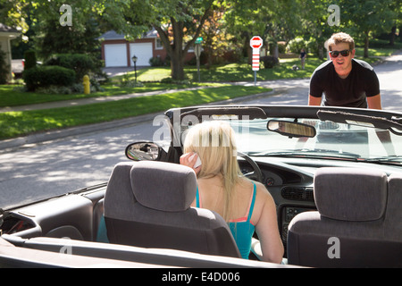 Se concentrer sur les jeunes femme faisant un téléphone cellulaire appel à l'aide tandis qu'un jeune homme ouvre le capot d'une voiture décapotable sur la route Banque D'Images