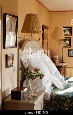 Gros coussins blancs sur un lit ancien avec détail sculpté dans une chambre avec du papier peint à motifs et des tables de chevet Banque D'Images