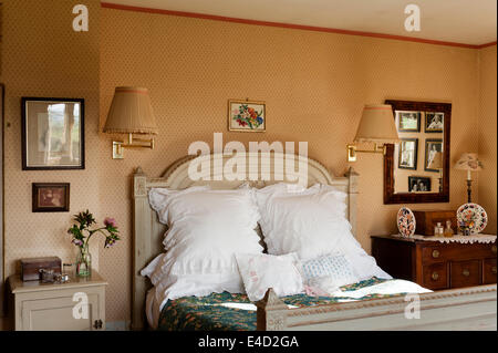 Gros coussins blancs sur un lit ancien avec détail sculpté dans une chambre avec du papier peint à motifs et des tables de chevet Banque D'Images