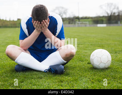 Déçu football player en bleu assis sur pitch après avoir perdu Banque D'Images