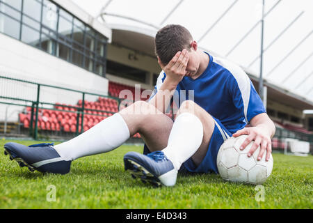 Déçu football player en bleu assis sur pitch après avoir perdu Banque D'Images