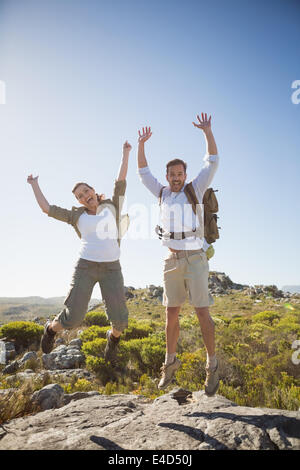 Couple de randonnée saut et acclamant terrain rocheux Banque D'Images