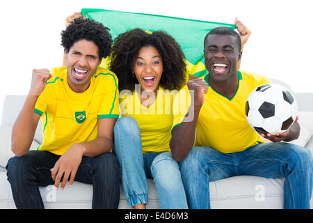 Heureux les fans de football en jaune assis sur table avec le drapeau du Brésil Banque D'Images