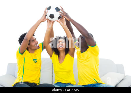 Heureux les fans de football en jaune sitting on couch with ball Banque D'Images