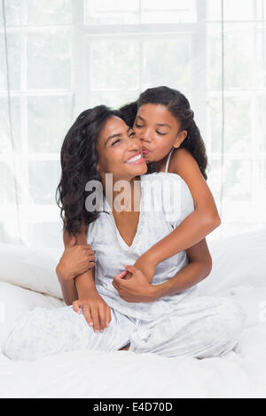 Smiling mother and daughter posing together on bed Banque D'Images