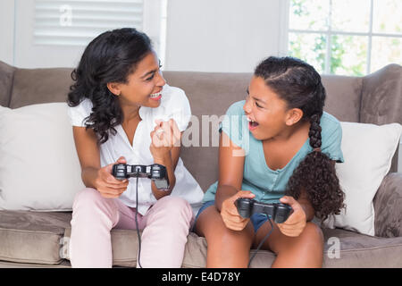 Happy mother and daughter playing video games ensemble sur canapé Banque D'Images