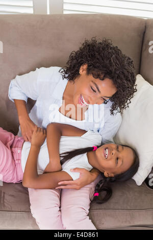 Jolie mère assise sur le canapé fille tickling Banque D'Images