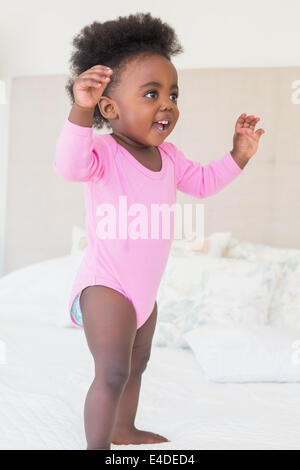 Petite fille en rose babygro standing on bed Banque D'Images