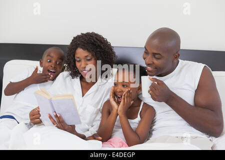 Family relaxing together in bed reading book Banque D'Images