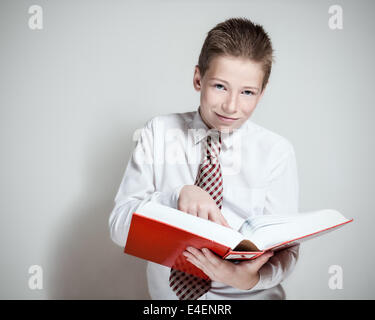 Le nice smiling boy lit un gros livre rouge sur fond gris Banque D'Images