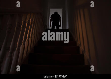 Silhouette d'un homme affalé dans le haut d'un escalier, les ombres projetées sur les murs de la lumière ci-dessous. Voir des photos similaires Banque D'Images