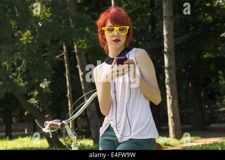 Hipster adolescente sur son vélo vintage, à écouter la musique sur son téléphone intelligent violet Banque D'Images