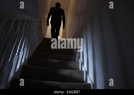 Silhouette d'un homme marchant à l'étage Vue arrière, les ombres projetées sur les murs de la lumière ci-dessous. Banque D'Images