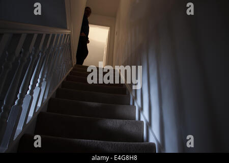 Silhouette d'un homme appuyé contre le mur en haut de l'escalier, des ombres projetées sur les murs de la lumière ci-dessous. Banque D'Images